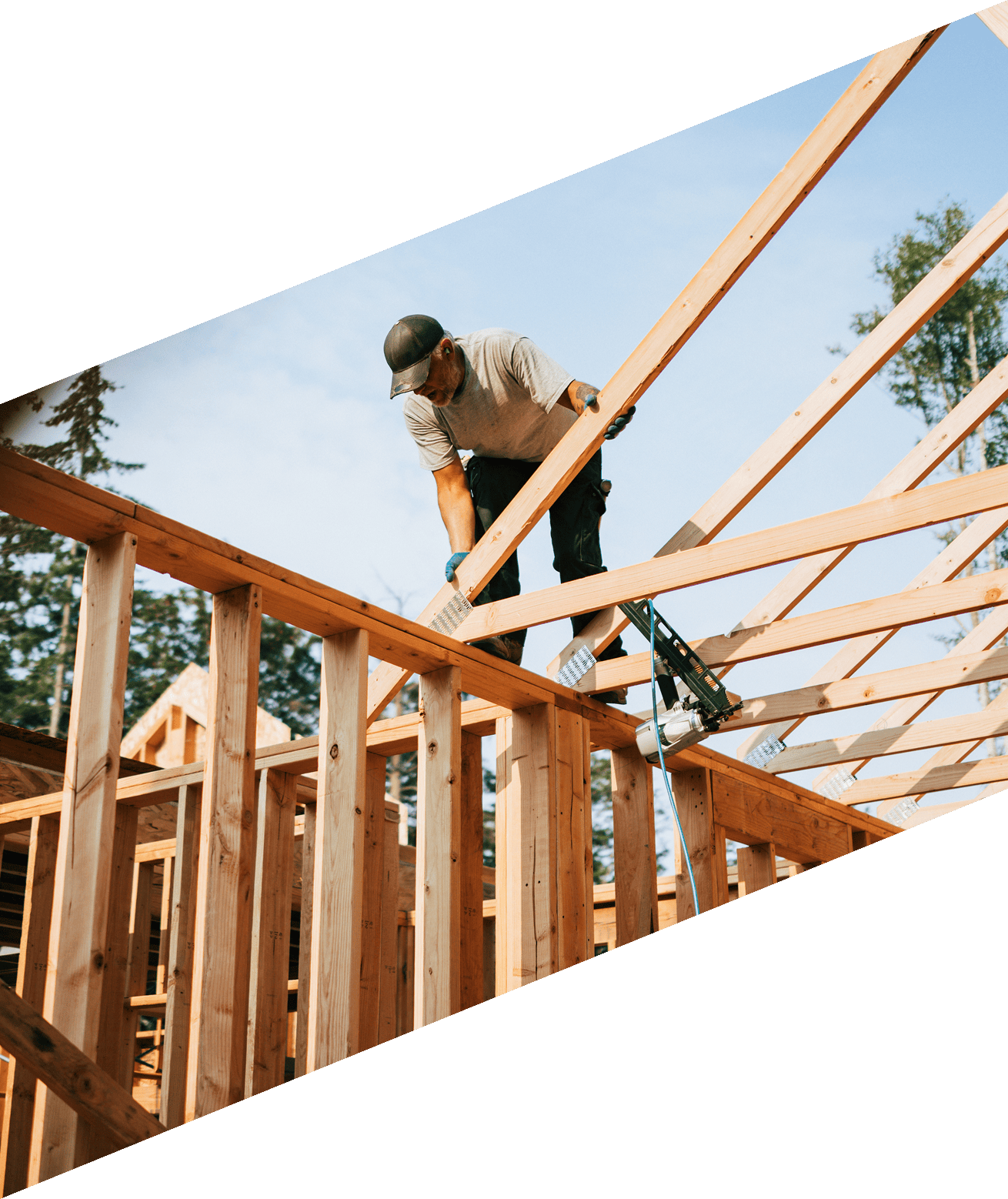 Man wearing a cap and holding a nail gun while working on a wooden structure