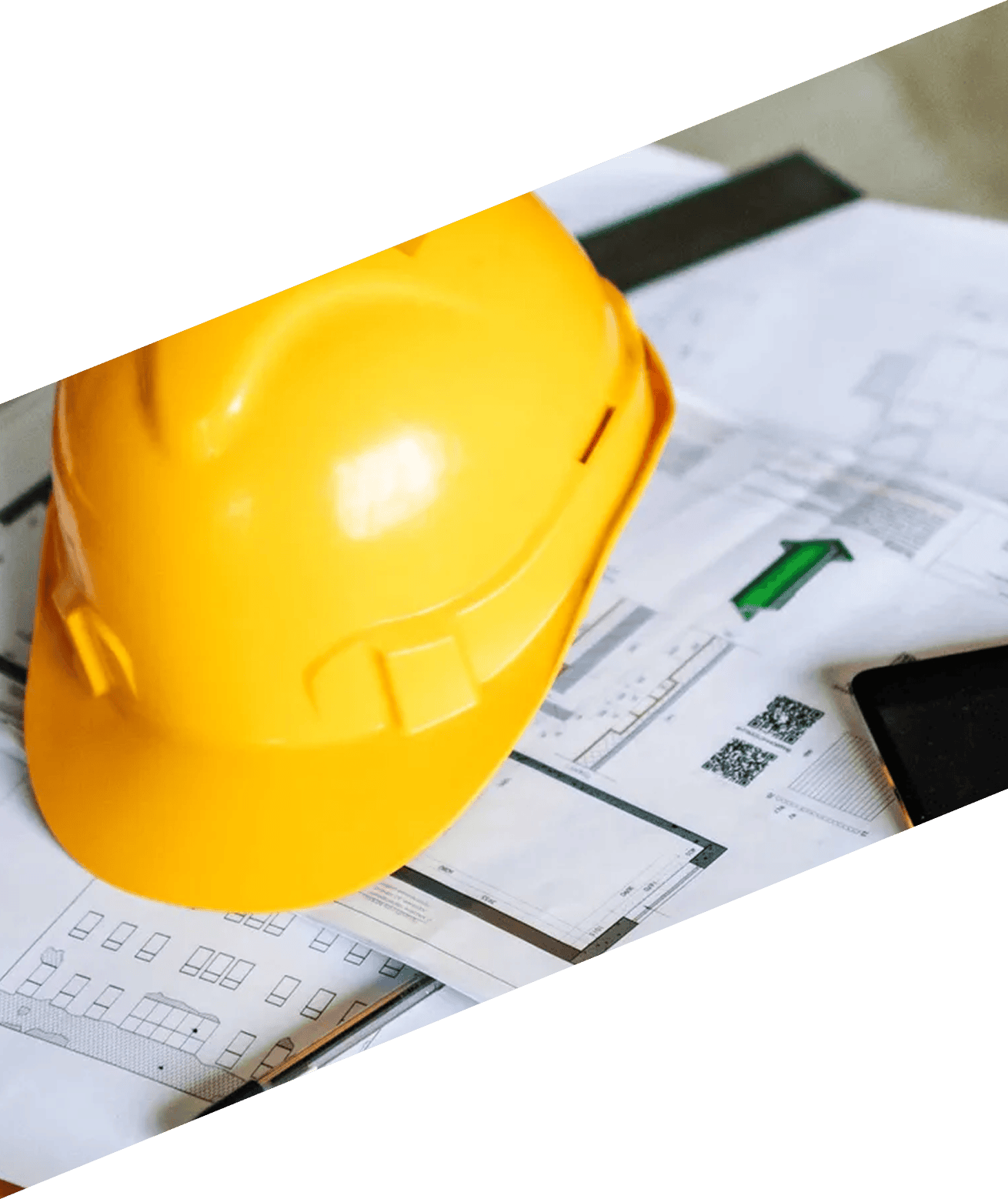 Yellow hard hat sitting atop a table, surrounded by blueprints and a mobile phone